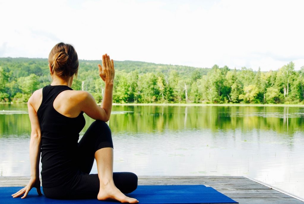 fit woman doing yoga facing a lake landscape during summer