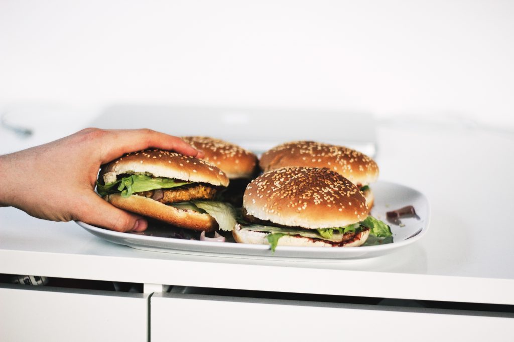 hand grabbing veggie burger on a plate with multiple burgers