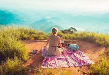 young woman having a picnic in front of scenic view of mountains