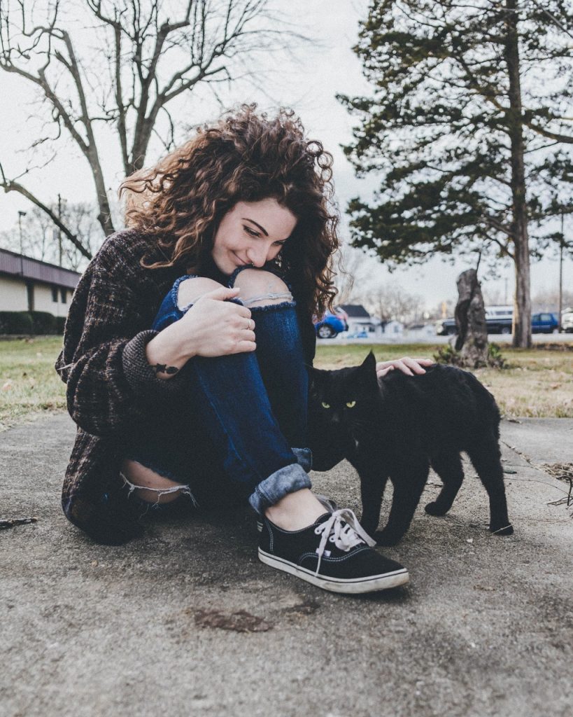 curly haired woman with black cat in a park