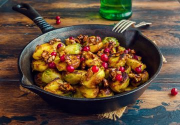 Roasted Brussels sprouts with caramelized walnuts and cranberries in a cast iron frying pan on a wooden table.