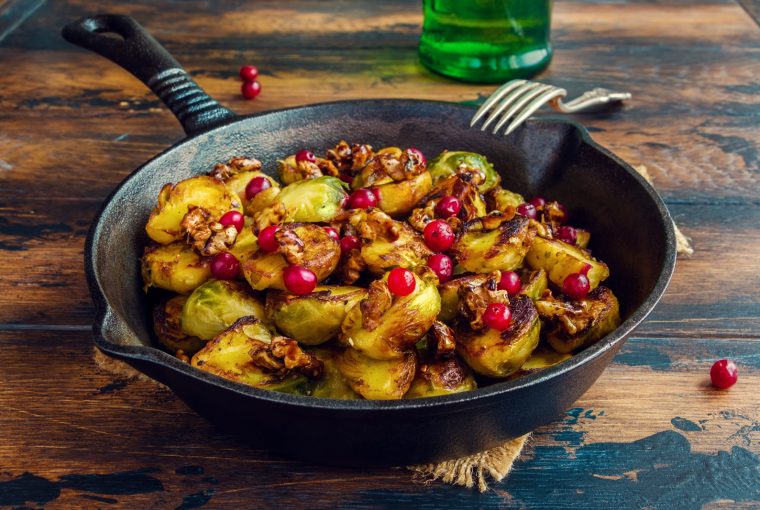 Roasted Brussels sprouts with caramelized walnuts and cranberries in a cast iron frying pan on a wooden table.