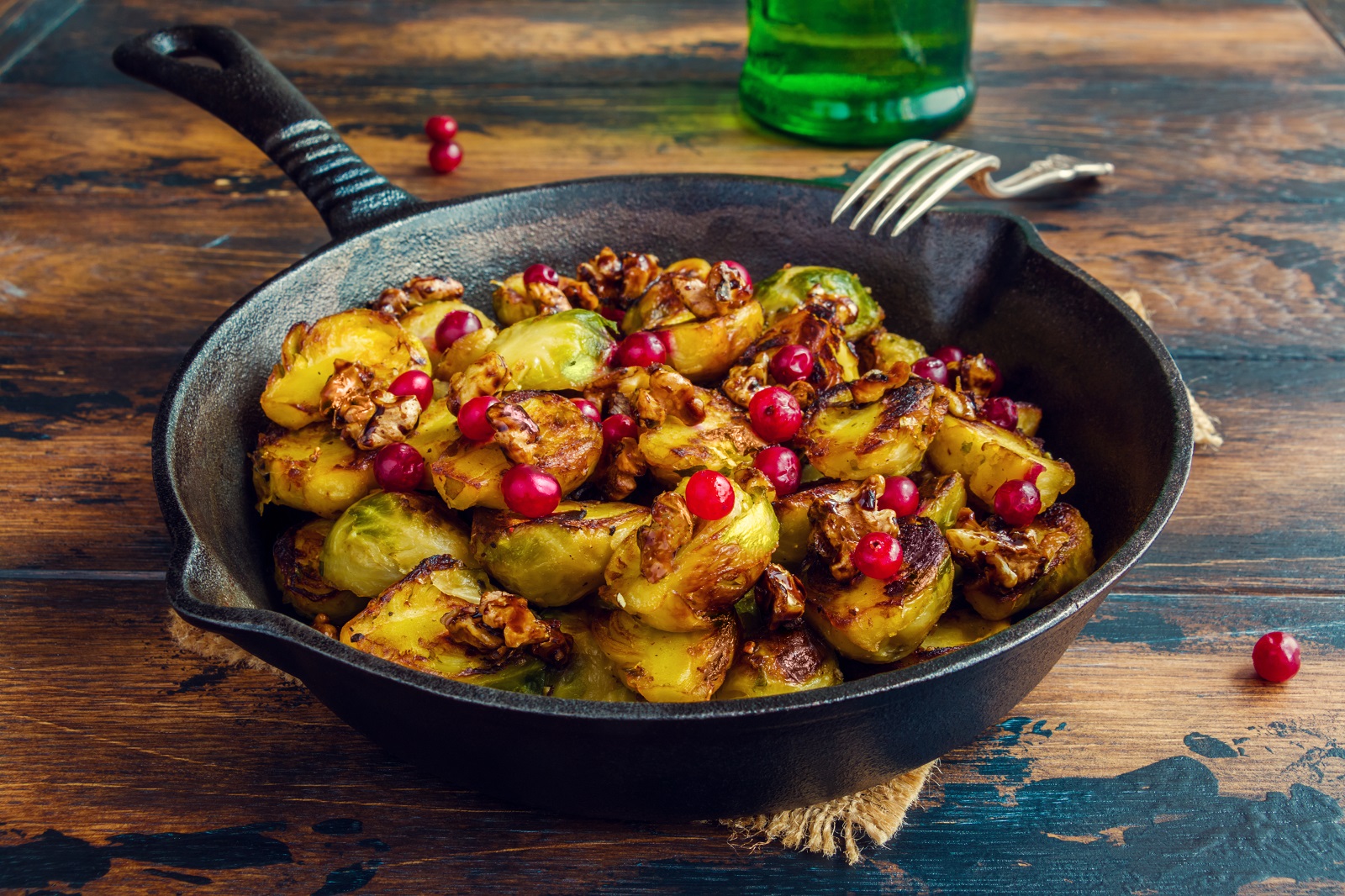 Roasted Brussels sprouts with caramelized walnuts and cranberries in a cast iron frying pan on a wooden table.