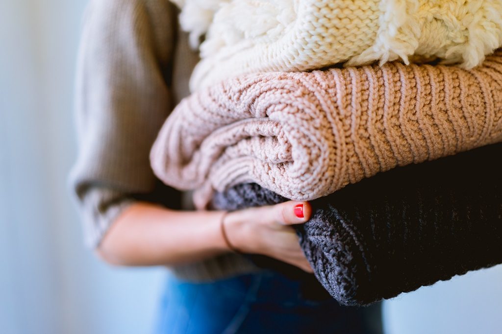 woman holding pile of sweaters