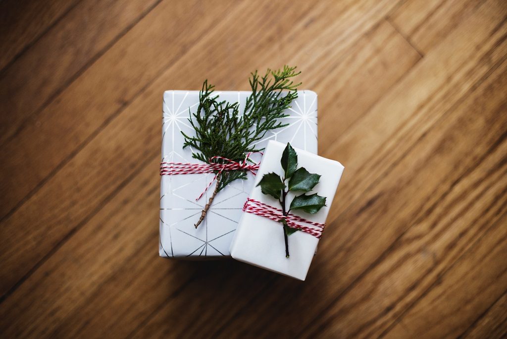 2 gifts wrapped in white paper and decorative foliage