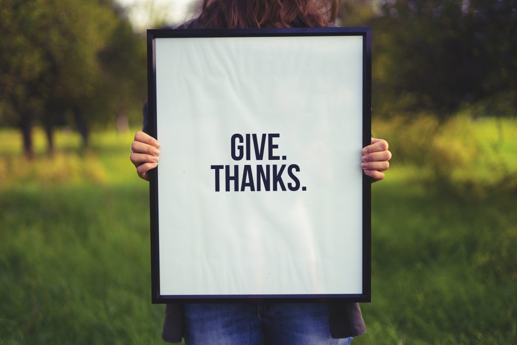 A woman holding a "give. thanks." poster 