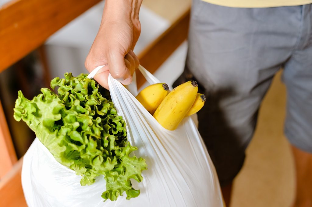 man carrying plastic grocery bag filled with fruits and veggies